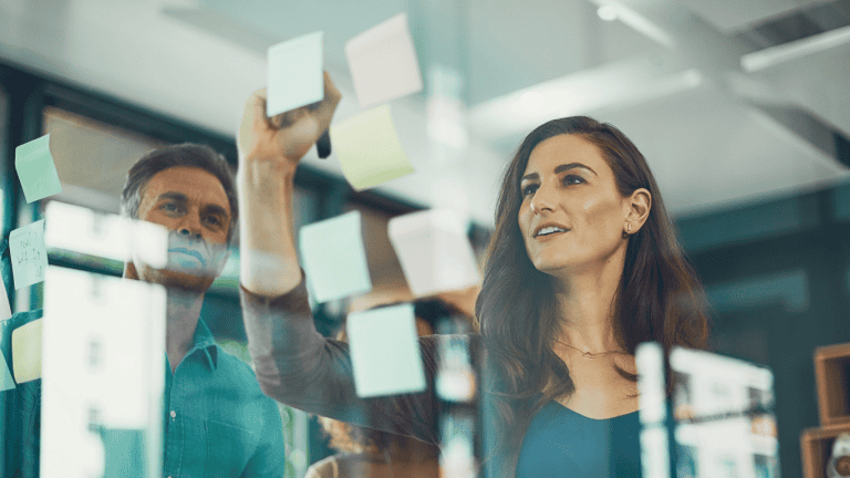 Woman and man create a talent recruitment strategies for a business organization by placing post-it notes on glass wall.